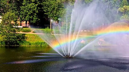 Wall Mural - rainbow in fountain spray over lake with trees in background