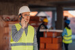 © Ljustina - Construction engineer wearing safety helmet and vest talking on smartphone at building site
