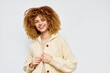 © SHOTPRIME STUDIO - Smiling young woman with curly hair in a cozy cream sweater against a plain white background, showcasing a warm and inviting fashion style perfect for autumn and winter