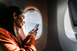 © Westend61 - Passenger using smartphone in airplane window seat during flight