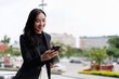 © crizzystudio - Smiling asian businesswoman using smartphone in urban setting