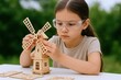 © The Little Hut - Focused Young Girl Building Wooden Windmill Model Wearing Safety Glasses Outdoors, STEM Education