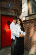 © Kirill Kleikov - Young married couple shares a warm embrace, standing together in front of a striking red door and textured brick wall