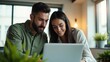 © MT Studio - A young couple looking at a laptop screen together in a bright room with plants and a window behind them
