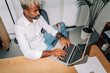 © Studio Marmellata - From above direct flash shot of Middle Eastern man in white shirt and ripped jeans typing and entering data into netbook while sitting near table and working in office.