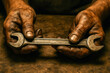 © Nargiz - Close-up photograph of gritty, hardworking hands holding a worn double-ended wrench over a stained workbench, symbolizing labor, resilience, the enduring strength of blue-collar workers on Labor Day