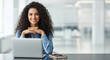 © Kamran - A confident businesswoman with curly hair smiles at her desk in a modern office. Perfect for representing approachable leadership and professionalism