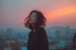 © Chalintara - Asian woman standing alone on a rooftop at sunset, peaceful and free, happy vibe, minimal urban background, soft wind in her hair