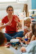 © lordn - Preschool teacher leading a diverse group of children in a fun music activity, playing instruments together in a circle.