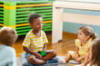 © lordn - Diverse preschool children sitting on the floor in a circle, engaged in group discussion and play, in a bright and cheerful classroom environment