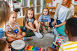 © lordn - Preschool teacher leading a music lesson, engaging children in rhythm and percussion activities during group playtime.