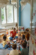 © lordn - Teacher engaging a diverse group of preschool children in a fun indoor activity, sitting together in a circle and developing social and learning skills in a cozy kindergarten classroom