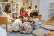 © lordn - Teacher engaging a diverse group of preschool children in a fun indoor activity, sitting together in a circle and developing social and learning skills in a cozy kindergarten classroom