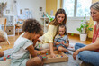 © lordn - Two preschool teachers with children sitting on floor, engaging in collaborative early learning activity in bright classroom