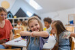 © lordn - Happy preschool girl smiling and posing at the table during creative classroom activities, surrounded by friends and a teacher in a bright, playful environment