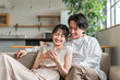 © buritora - 家のリビングでスマホを見る仲良しの若い日本人夫婦（スキンシップ）