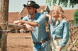 © Teodor Lazarev - Couple dressed in denim stands near a fence on a sunny farm. The cowboy leans casually while the model enjoys the warm weather, capturing the essence of rural fashion