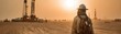 © pingpao - A worker stands in a desert landscape near drilling equipment, bathed in golden sunlight, highlighting the harsh conditions of the environment.