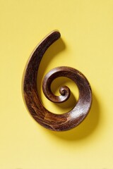 Poster - A close up shot of a dark brown wooden spiral on a yellow background showing the texture of the wood