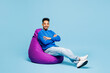 © ViDi Studio - Full body young man of African American ethnicity wears sweatshirt casual clothes sit in bag chair look camera isolated on plain pastel light blue cyan background studio portrait. Lifestyle concept.