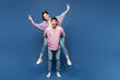 © ViDi Studio - Full body young couple two friends family man woman they wear pink casual clothes together giving piggyback ride to joyful, sit on back show v-sign isolated on plain blue background Lifestyle concept