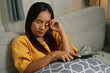 © Johnstocker - Top view, Middle-aged Asian woman relaxes on the sofa, looking drowsy while watching a movie in the living room at home.