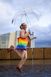 © asier - Happy businesswoman jumping with rainbow bag and transparent umbrella