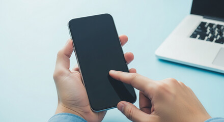 Wall Mural - close-up of hands holding smartphone with blank screen, finger interacting, laptop blurred backgroun