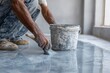 © Abba - Man painting floor with gray epoxy paint with bucket and brush. Shows home improvement, new builds, and commercial construction.