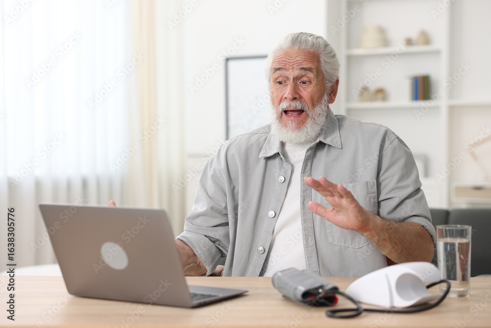 Senior man having online consultation with doctor via laptop at table indoors