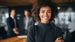 © Johannes - confident young african businesswoman standing with folded arms smiling at the camera in a boardroom with male colleagues in the background no logos no brands ar 169