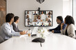 © fizkes - Modern tech innovation for business communication. Diverse multiracial team collaborate during hybrid online and in person meeting for briefing event interact both at conference table and by videocall