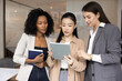 © fizkes - Informal idea sharing and casual teamwork. Three beautiful young women coworkers from diverse ethnic groups meet in office stand together talk engaged in creative brainstorming collaborate with tablet