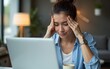 © fu - Focused young businesswoman looking at laptop pc computer screen having headache, migraine. Latin business woman holding hand near temples, feeling stressed and tired sitting at workplace in office
