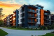 © Khusi - Modern residential apartment complex with orange and gray exterior during vibrant sunset with landscaped green lawns and paved walkways