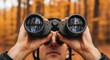 © PLATİNUM - A man peers through binoculars, enjoying the autumn forest view with trees reflecting in the lenses.