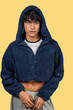 © EDUARDOIVAN - Young man wearing blue furry cropped hoodie and grey sweatpants posing on yellow background