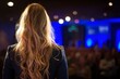 © Sea Lily - Woman speaker with long blonde hair on stage talking to audience. Business meeting, conference or seminar. Public speaking concept.
