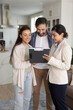 © fizkes - Real estate agent showing document to couple, discussing details of property, reviewing listing or contract, standing in modern flat. Designer demonstrate interior design ideas to clients on clipboard