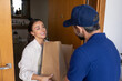 © fizkes - Young 30s Caucasian woman interacting with male courier stands on doorway house porch, takes two big paper bags with ordered foodstuff. E-commerce fulfillment, food takeaway services, grocery delivery