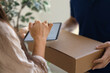 © fizkes - Close up cropped photo of woman holding digital tablet and signing receipt as male courier delivers package with ordered goods to her doorsteps. Comfortable, excellent delivery services, acceptance