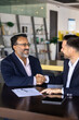 © fizkes - Happy business project buyer and seller men shaking hands, sitting at work table with documents, meeting for cooperation, partnership, getting agreement about investment. Vertical shot