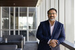 © fizkes - Happy successful older Indian business leader man in glasses and formal clothes posing in office lobby space alone, looking at camera, smiling. Successful mature CEO, executive professional portrait