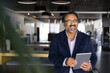 © fizkes - Cheerful elder Indian businessman using tablet computer, looking away, smiling, laughing. Senior executive holding gadget in co-working office, thinking on Internet technology for business success
