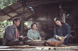 © pichet - Traditional Asian Family Cooking in Rural Setting with Generational Bonding, Women Preparing Ingredients, and Men Engaged in Conversation