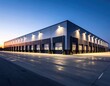 © Amira - Modern industrial warehouse exterior at dusk with illuminated facade and clear sky