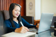 © panomporn - Smiling young Asian student wearing headphones talking on online chat using laptop.