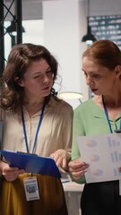 Poster - Vertical Video Ambitious and goal oriented diverse businesswomen reviewing corporate reports and graphs, working in synergy to achieve professional growth in a modern work environment. Camera B.