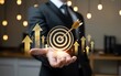 © Sb - Businessman holds a virtual interface with a golden target hit by an arrow, representing achieving business goals, strategic success, and corporate development with upward growth.