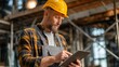© benjamin - A focused construction worker in a yellow hard hat reviewing paperwork. He is standing in a large industrial building, possibly a warehouse or factory.